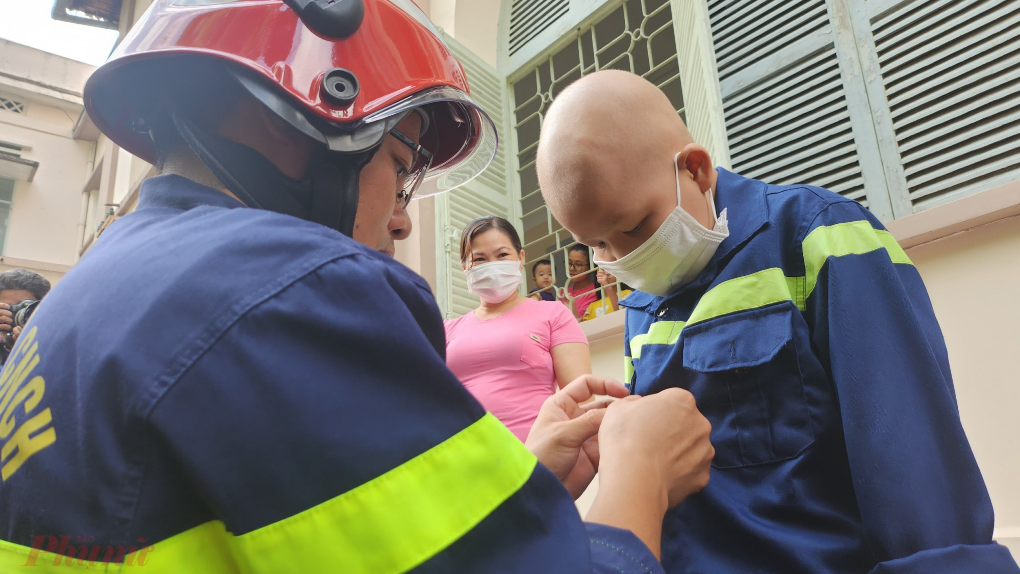 Đại úy Đỗ Ngọc Đức - Bí thư Đoàn thanh niên Cảnh sát Phòng cháy chữa cháy và cứu nạn cứu hộ Công an TPHCM - trang bị trang phục lính cứu hỏa cho bé Quân: