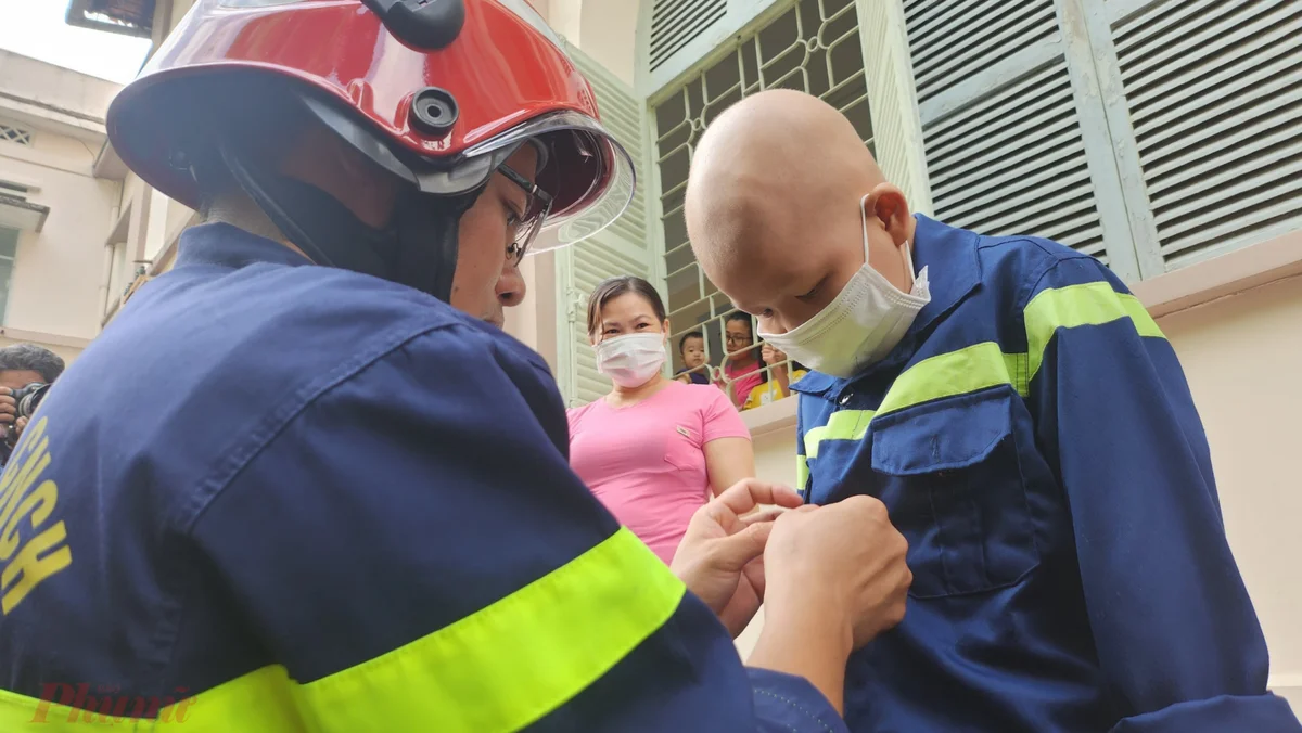 Đại úy Đỗ Ngọc Đức - Bí thư Đoàn thanh niên Cảnh sát Phòng cháy chữa cháy và cứu nạn cứu hộ Công an TPHCM - trang bị trang phục lính cứu hỏa cho bé Quân: