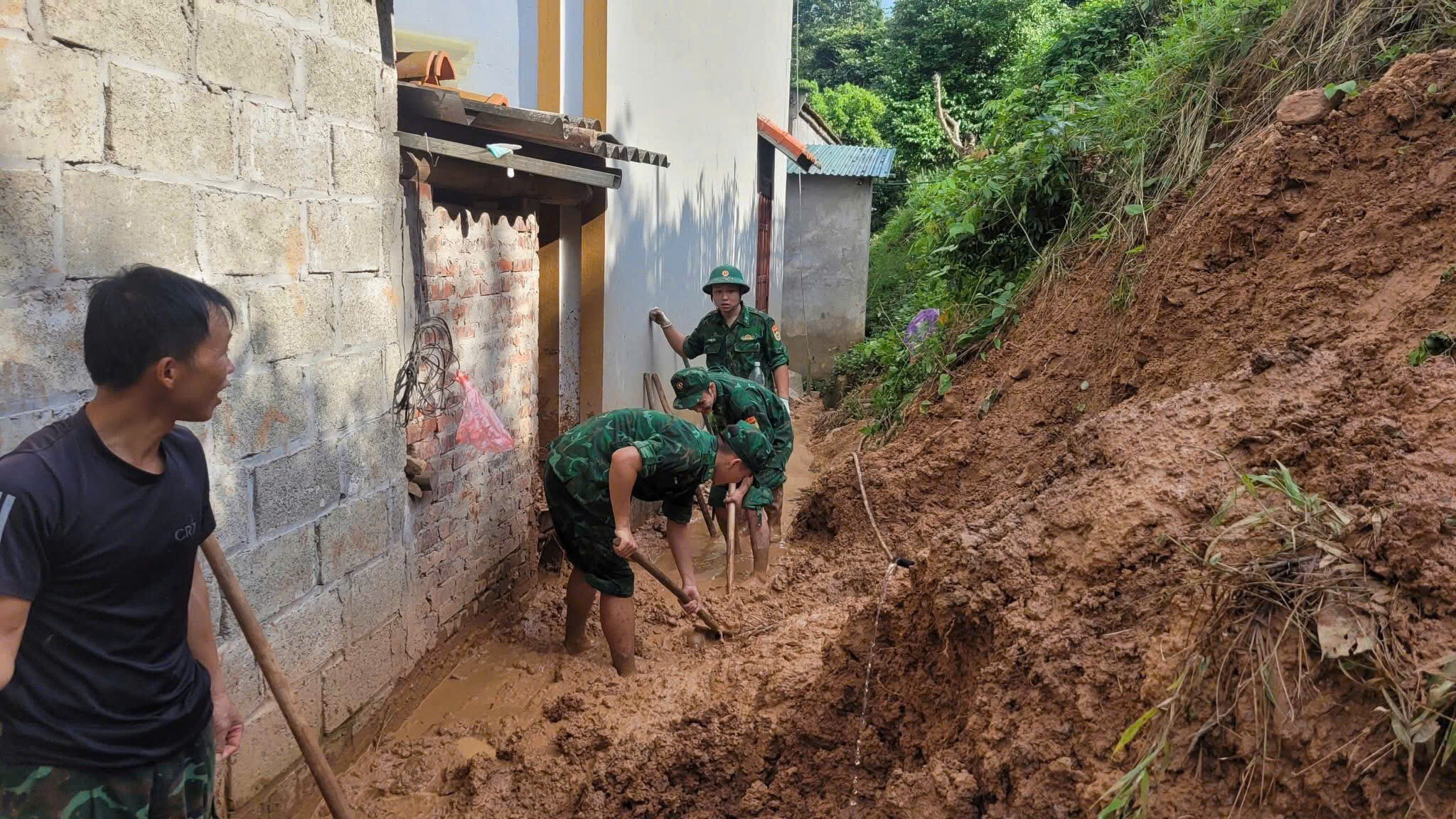 Các cán bộ chiến sĩ, cùng người dân xử lý điểm sạt nở đất xuống khu vực nhà đảm bảo an toàn.